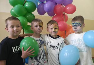 Chłopcy z pomalowanymi buziami trzymają balony.