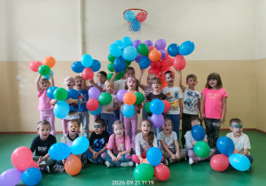 Przedszkolaki z pomalowanymi twarzami trzymają kolorowe balony.