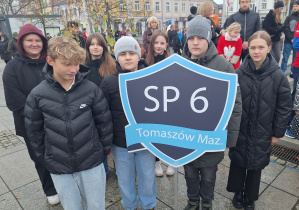 Uczniowie klasy VIIa stoją z tarczą Szkoły podczas uroczystości.