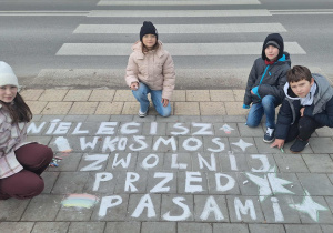Uczniowie kucają na chodniku przy swoim haśle.