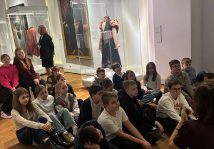 Uczniowie siedzą i słuchają prowadzącej w czasie zajęć w Muzeum Narodowym.