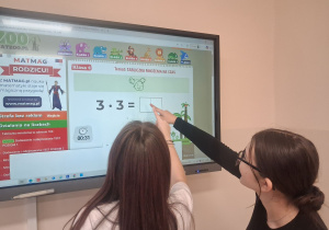 Uczennice rozwiązują zadania na ekranie multimedialnym.