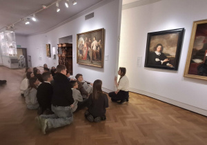Uczniowie siedzą przed obrazem w Muzeum Narodowym.