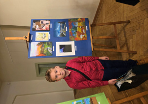 Filip stoi przy wystawie nagrodzonych prac.