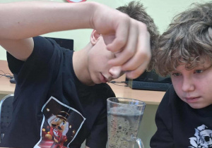 Uczniowie mieszają różne substancje w szklance.