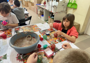 Dzieci pracują nad ozdabianiem bombek.