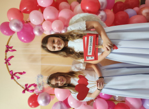 Dziewczynki przebrane za anioły pozują przy ściance z balonów.