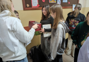 Członkinie Szkolnego Klubu Wolontariatu trzymają pudełko do losowania wyzwań.