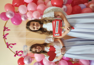 Dziewczynki przebrane za anioły stoją przy ściance z balonów.