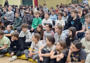 Uczniowie klas IV-VIII siedzą podczas spotkania.