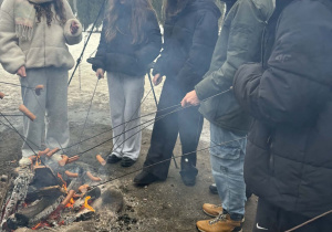 Siódmoklasiści pieką kiełbaski przy ognisku.