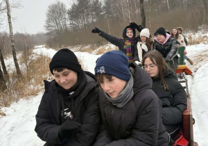 Uczniowie jadą saniami przez las.