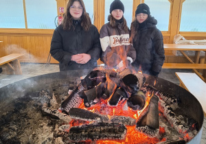 Dziewczynki grzeją się przy palenisku.