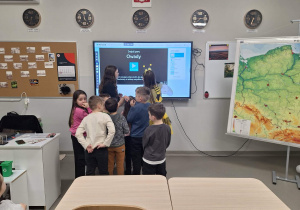 Dzieci z pomocą starszych koleżanek korzystają z tablicy multimedialnej.