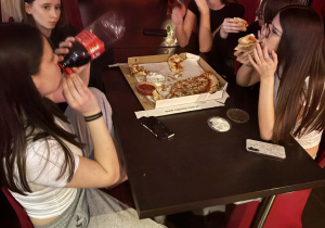 Dziewczynki jedzą pizzę i piją colę.