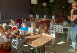 Przedszkolaki siedzą przy stołach w pizzerii.