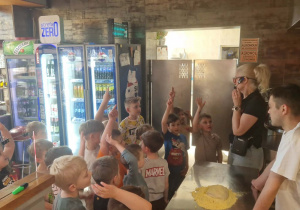 Dzieci w pizzerii zgłaszają się do udzielenia odpowiedzi na pytanie.