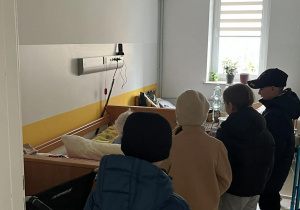 Dzieci stoją obok łóżek seniorów w ZPO.
