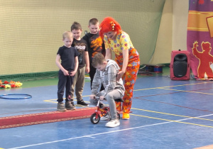 Jeden z chłopców próbuje jeździć z pomocą klauna na mini rowerku.