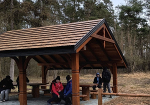 Uczestnicy wyprawy odpoczywają pod drewnianą wiatą.