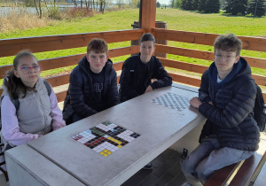 Uczniowie siedzą w drewnianej altanie.