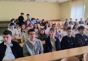 Uczniowie klas siódmych siedzą przed wykładem.