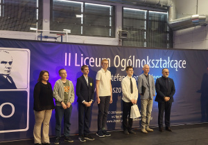 Mikołaj Więckowski stoi wśród innych wyróżnionych w konkursie oraz organizatorów.