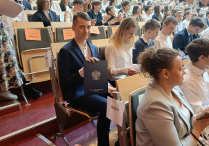 Piotrek siedzi i pokazuje otrzymane zaświadczenie.