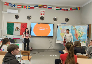 Goście stoją przy tablicy przed uczniami klas siódmych.