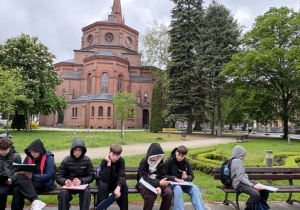 Uczniowie siedzą na ławkach i rozwiązują zadania podczas gry miejskiej.