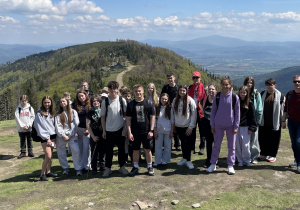 Uczestnicy wycieczki stoją na tle panoramy Beskidów.