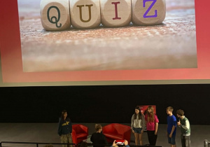 Uczniowie klas siódmych stoją przed widownią i rozwiązują Quiz.