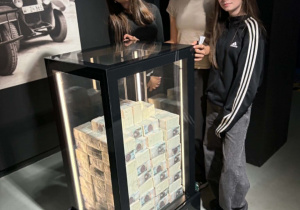 Dziewczyny stoją przy gablocie z banknotami.