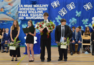 Uczniowie stoją z kwiatami i dziękują za wspólnie spędzony czas.