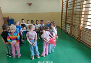 Dzieci podają sobie za plecami balon w sali gimnastycznej.