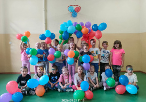 Przedszkolaki z pomalowanymi twarzami trzymają kolorowe balony.