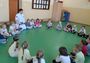Dzieci siedzą w kole w sali gimnastycznej razem z prowadzącym pokazowe zajęcia z taekwondo.