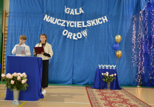 Prowadzący uroczystość stoją przed publicznością.