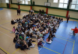 Zdjęcie wykonane z góry na uczniów siedzących w hali sportowej na spotkaniu z p. Marianem Woroninem.