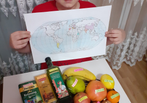 Uczeń klasy VIb pokazuje produkty spożywcze oraz mapę świata z krajami, z których pochodzą te produkty