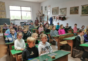 Uczniowie siedzą w ławkach w dawnej sali lekcyjnej