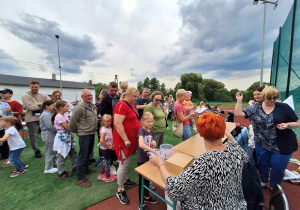 Dzieci z rodzicami stoją w kolejce po losy na loterię fantową