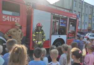 Strażak prezentuje dzieciom ubranie używane przy gaszeniu pożaru