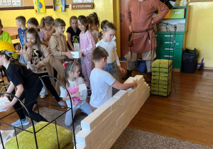 Pierwszoklasiści budują mur ze styropianowych cegiełek w klasie.