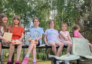 Dziewczynki siedzą na trybunach przy boisku.