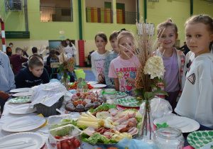 Uczniowie klasy IIa stoją wokół stołu śniadaniowego.