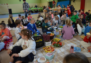Uczniowie klas I- III jedzą śniadanie siedząc na kocach.