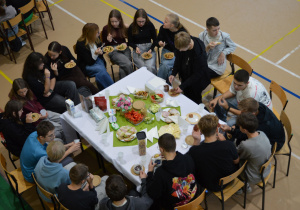Klasa VIIIa siedzi wokół stołu i je śniadanie.