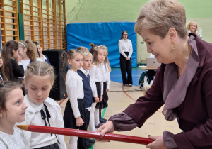 Pani Dyrektor Wydziału Edukacji Iwona Sudak pasuje ołówkiem uczennicę klasy pierwszej.