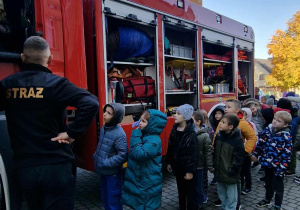Dzieci stoją przed wozem strażackim.